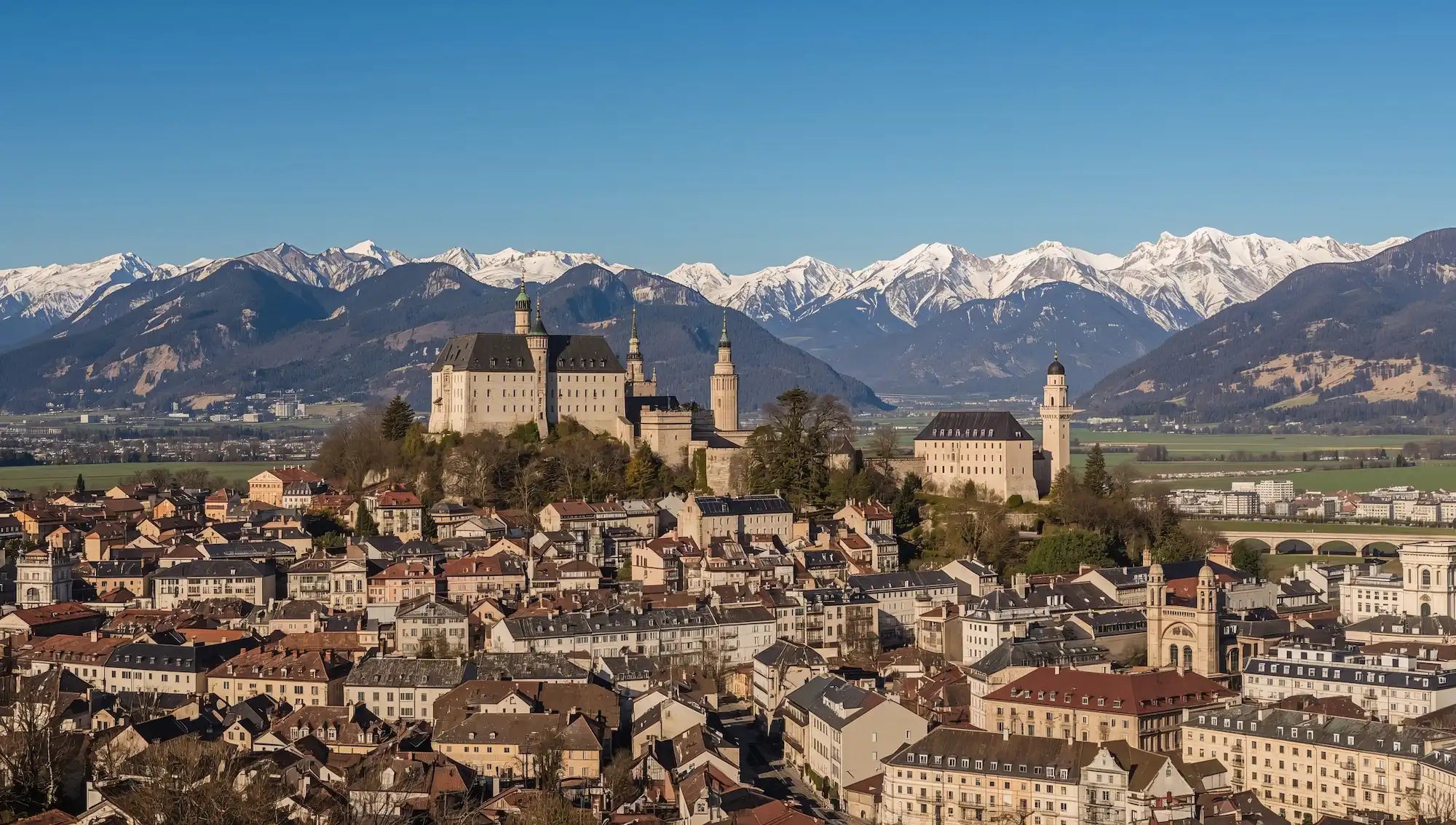 Vue aérienne de la ville de Sion dans le canton du Valais avec ses châteaux et les Alpes en arrière-plan, zone couverte par KM Étanchéité.